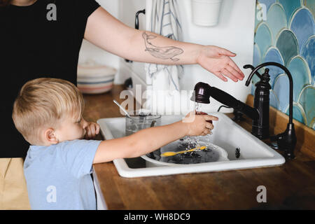 Kleiner Junge Pfirsich waschen in der Küche mit seiner Mutter helfen Stockfoto
