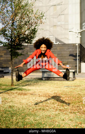 Porträt der glückliche junge Frau mit modischen roten Hosenanzug springen in die Luft, Stockfoto