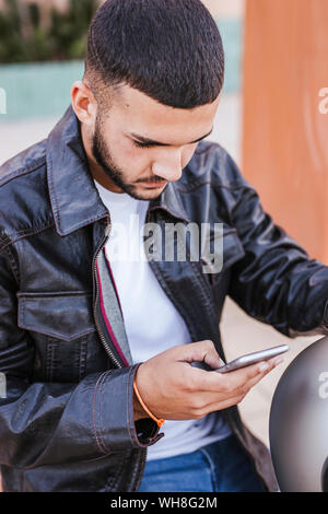 Junge Mann sitzt auf seinem Motorrad mit Handy Stockfoto