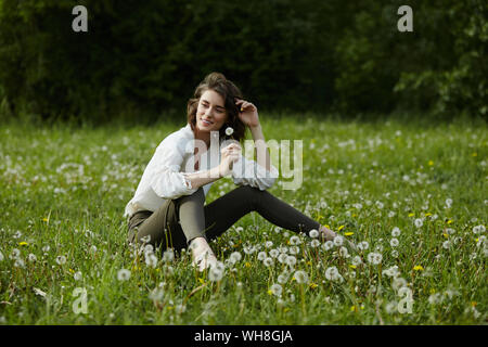 Frühling Portrait eines Mädchen sitzen in einem Feld auf dem Gras unter den Löwenzahn Blumen. Fröhliches Mädchen genießt sonnige Wetter im Frühling. Natürliche Schönheit einer woma Stockfoto