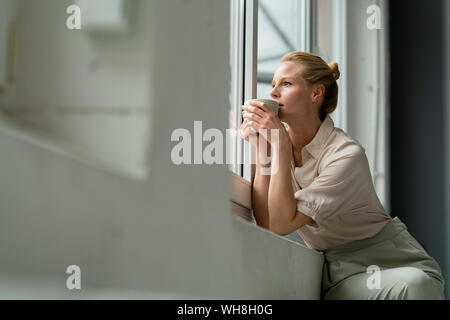 Junge Geschäftsfrau mit Tasse Kaffee Blick aus Fenster Stockfoto