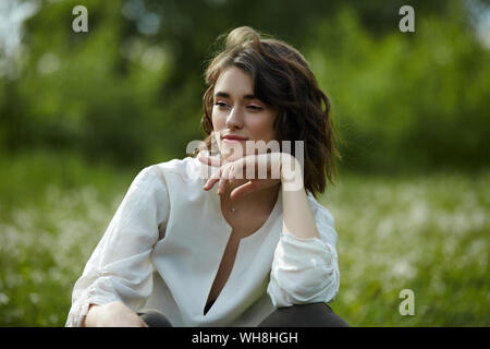 Frühling Portrait eines Mädchen sitzen in einem Feld auf dem Gras unter den Löwenzahn Blumen. Fröhliches Mädchen genießt sonnige Wetter im Frühling. Natürliche Schönheit einer woma Stockfoto