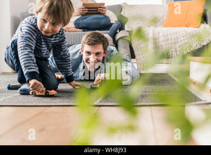 Vater und Sohn spielen mit Spielzeug Autos, liegend auf dem Boden Stockfoto