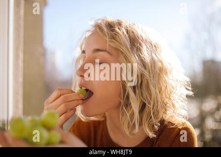 Porträt der blonde junge Frau Grün essen Trauben Stockfoto