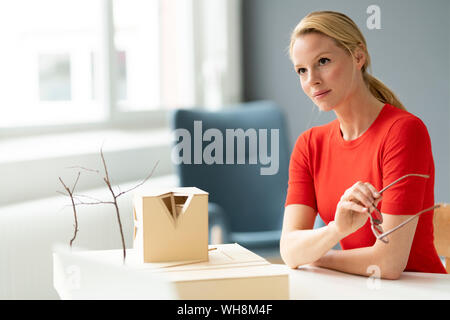 Nachdenkliche junge Frau im Büro mit architektonischen Modell auf dem Schreibtisch Stockfoto