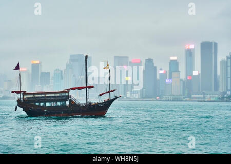 Blick auf den Victoria Harbour mit Segelschiff im Vordergrund, Hongkong, China Stockfoto