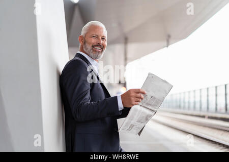 Gerne reife Geschäftsmann mit Zeitung, die sich am Bahnsteig Stockfoto
