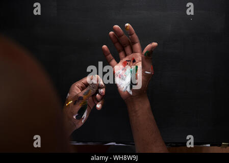 Die schmutzigen Hände der Künstler mit bunten Farben auf schwarzem Hintergrund Stockfoto