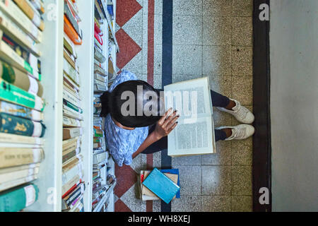 Blick von oben auf die junge Frau auf dem Boden sitzend, ein Buch in der Nationalbibliothek, Maputo, Mosambik Stockfoto