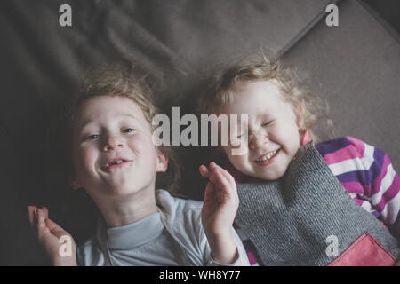 Porträt von zwei kleinen Schwestern nebeneinander auf der Couch liegend, Spaß, Ansicht von oben Stockfoto