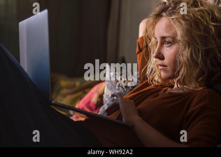Porträt der blonde junge Frau auf dem Bett liegend mit Laptop Stockfoto