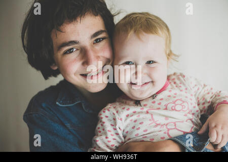 Portrait von Happy Teenager seine toddler Schwester umarmen Stockfoto
