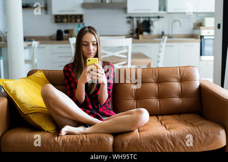 Junge Frau mit Handy auf der Couch zu Hause Stockfoto