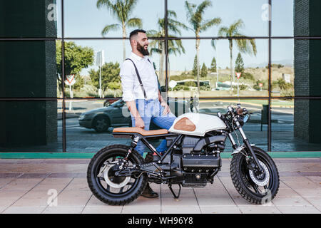 Mann mit Motorrad stand vor der Glasfassade. Stockfoto