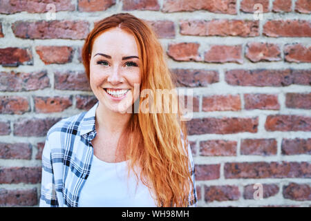 Porträt der schönen jungen Frau an der Kamera vor der Mauer lächelnd Stockfoto