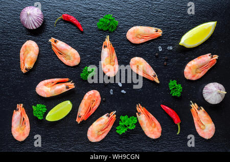 Essen Hintergrund mit gekochten Garnelen, Chili, Knoblauch und Zitrone auf schwarzem Hintergrund Stockfoto