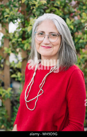 Portrait von lächelnden älteren Frau mit grauem Haar zu tragen rote Pullover und Gläser Stockfoto