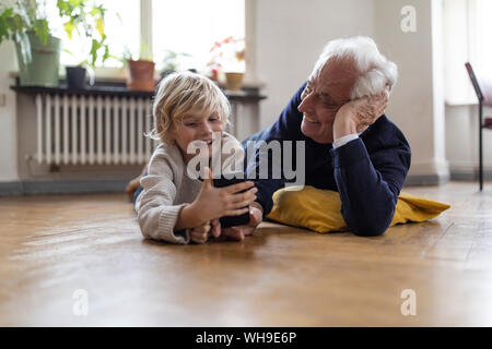 Großvater und Enkel zu Hause auf dem Boden liegend mit einem Smartphone Stockfoto