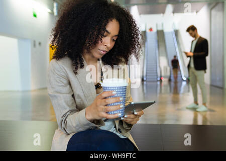 Junge Geschäftsfrau mit Takeaway Kaffee und Smartphone in einem Foyer Stockfoto