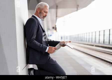 Reifen Geschäftsmann lesen Zeitung, die sich am Bahnsteig Stockfoto