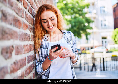 Junge Frau lehnte sich gegen die Mauer in der Stadt, während Sie ihr Smartphone Stockfoto