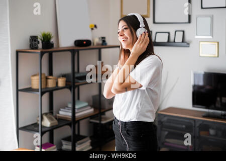 Glückliche junge Frau zu Musik über Kopfhörer zu Hause Stockfoto