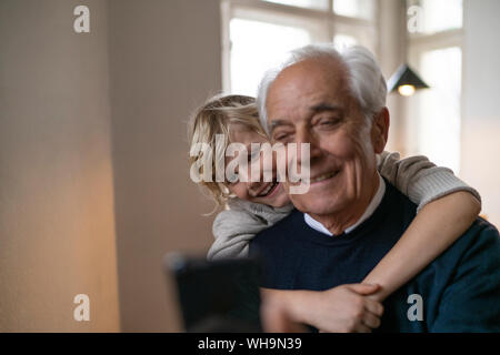 Happy Enkel umarmen Großvater mit Handy zu Hause Stockfoto