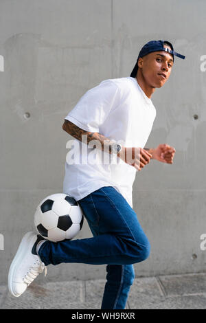 Portrait von tätowierten jungen Mann balancing Fußball vor der Betonwand Stockfoto