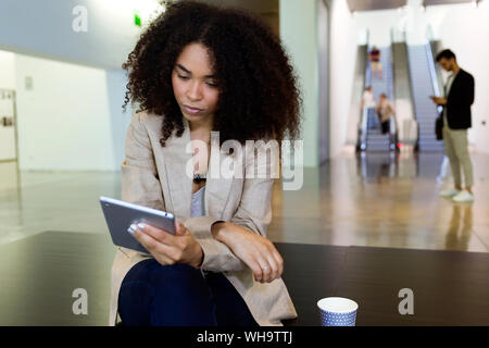 Junge Geschäftsfrau mit Tablet takeaway Kaffee in einem Foyer Stockfoto