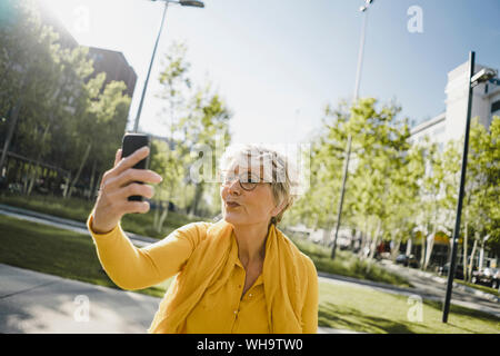 Portrait von reife Frau tragen gelbe Kleidung unter selfie mit Smartphone schmollend Mund Stockfoto