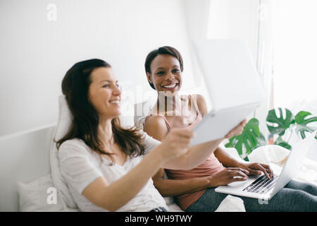 Zwei glückliche Frauen zu Hause im Bett liegend mit Laptops Stockfoto