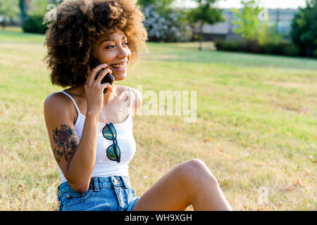 Porträt der glückliche junge Frau am Telefon sitzen auf einer Wiese