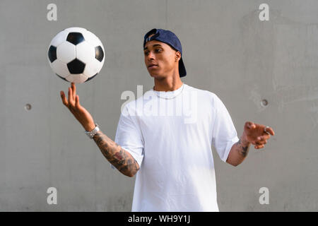 Portrait von tätowierten jungen Mann balancing Fußball auf seinen Finger vor der Betonwand Stockfoto