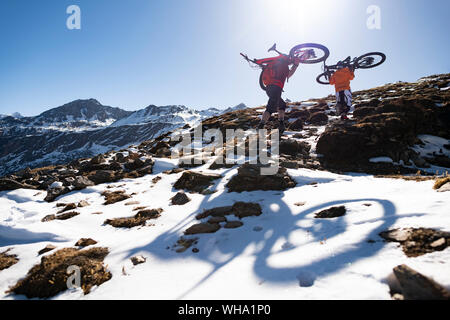 Mountainbiker tragen ihre Bikes auf einem schneebedeckten Hang in der Nepal Himalaya mit Blick auf den Langtang Gebirges, Nepal, Asien Stockfoto