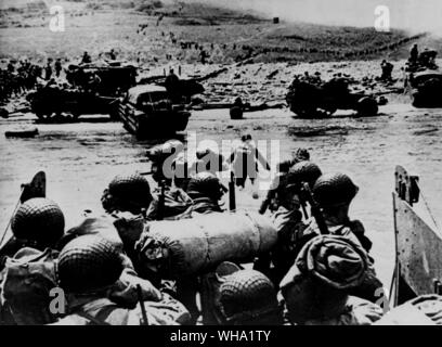 WW2: D-Tag. Amerikanische stoßtruppen von einem Landing Craft durch das flache Wasser auf einen Strand - Kopf im nördlichen Frankreich während der Landung der Alliierten. Hälfte - Titel und ein Strände DUKW am Strand - Kopf. Der Rauch im Hintergrund ist von naval Geschützfeuer Unterstützung der Angriff. 6. Juni 1944. Stockfoto