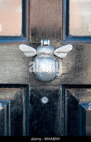 Glänzendes Metall Türklopfer in Form eines geflügelten Insekten auf einem Schwarz lackiert Tür mit Spion Linse unten Stockfoto