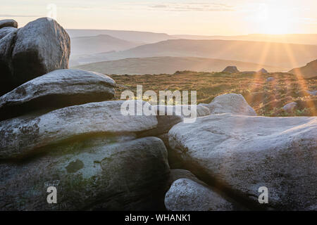 Sunset Landschaft im Peak District, England. Felsbrocken durch Sonnenlicht und Sonne über Hügel im Hintergrund beleuchtet. majestätischen Landschaft des ländlichen England. Helle Szene. Stockfoto