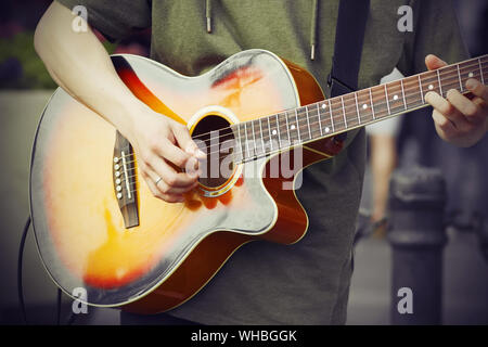 Ein Kerl in einem grünen Hoodie spielt eine traurige Melodie mit einem Mediator auf einem hellen Akustik Gitarre. Stockfoto