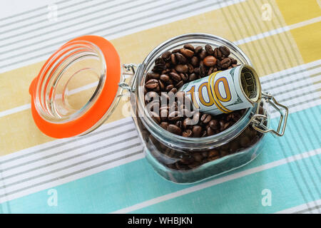 Rolle mit einem Hundert-euro-Scheine in einem Clip top Glas Glas mit Kaffeebohnen auf eine Tischdecke. Für Schüttgut Lebensmittel als Cache oder Safe. Stockfoto