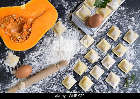 Frische Kürbis und Cottage cheese Ravioli mit Mehl auf einem dunklen Hintergrund. Prozess des italienischen Ravioli. Horizontale Ansicht von oben mit der Kopie Raum Stockfoto