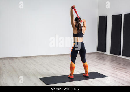 Portrait von athletischen Körper Fitness Mädchen in schwarz und orange Leggings führt Übungen für die Rückenmuskulatur und Hände mit Widerstand Band Stockfoto