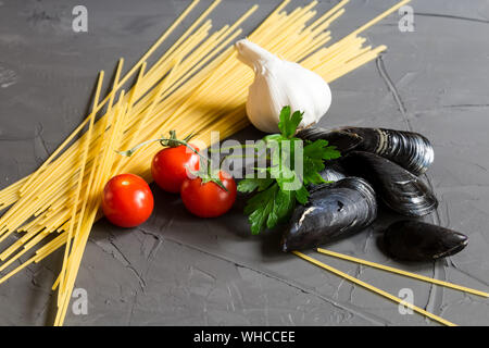 Frische Zutaten zum Kochen Meeresfrüchte Pasta - Zusammensetzung der spaghetti, Muscheln, Tomaten, Knoblauch und Petersilie auf grauem Hintergrund Stockfoto
