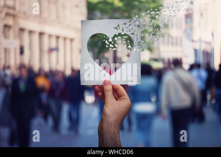 Gesundheit und Wohlbefinden globales Problem, wie die menschliche Hand hält ein Papier mit Herz in Stücke auf einer belebten Straße Hintergrund zu brechen. Leiden myo Stockfoto