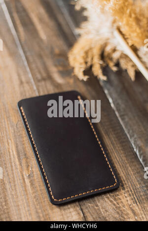 Teuer, schönes Cover von eco-Leder auf einem Hintergrund von Holz und Weizen. Schöne Natur Care Concept. Handgefertigte Phone Case in der Farbe schwarz. Stockfoto