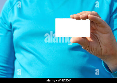 Ein Mann in Blau mit langer Hülse hält eine Visitenkarte oder eine Ankündigung in der Hand, mockup Stockfoto