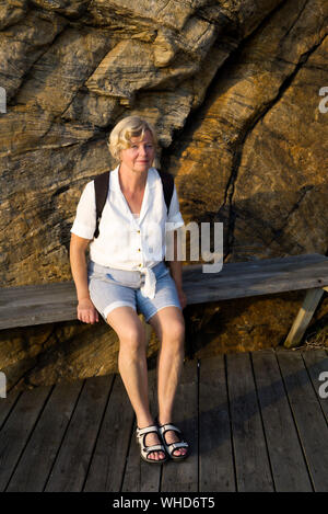 Blonde Frau entspannend auf einer Bank am Hafen in Smögen an einem sonnigen Herbst Abend Stockfoto