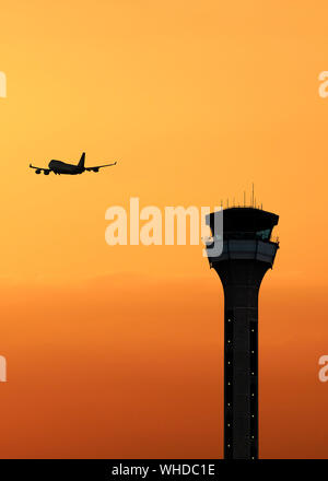 Air Traffic Control Tower mit einem Flugzeug, die bei Sonnenuntergang Stockfoto