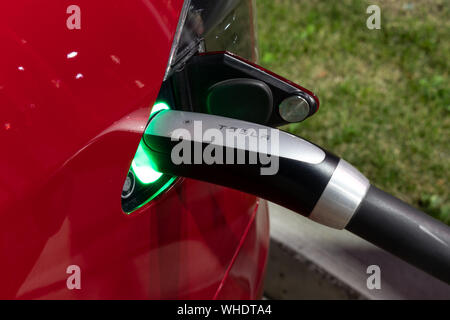 Tesla Supercharging Kabelgriff gesehen, während angeschlossen an roten Tesla in der Nacht. Stockfoto