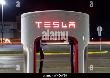 Tesla Supercharger Station mit aufgehängten Ladekabel bei Nacht gesehen. Stockfoto