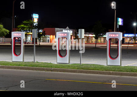 Drei Tesla-Supercharger-Stationen, die spät in der Nacht vor einer verkehrsreichen Straße gesehen wurden. Stockfoto